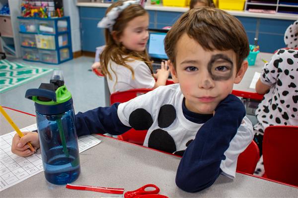boy dressed as dalmatian dog with water bottle on desk